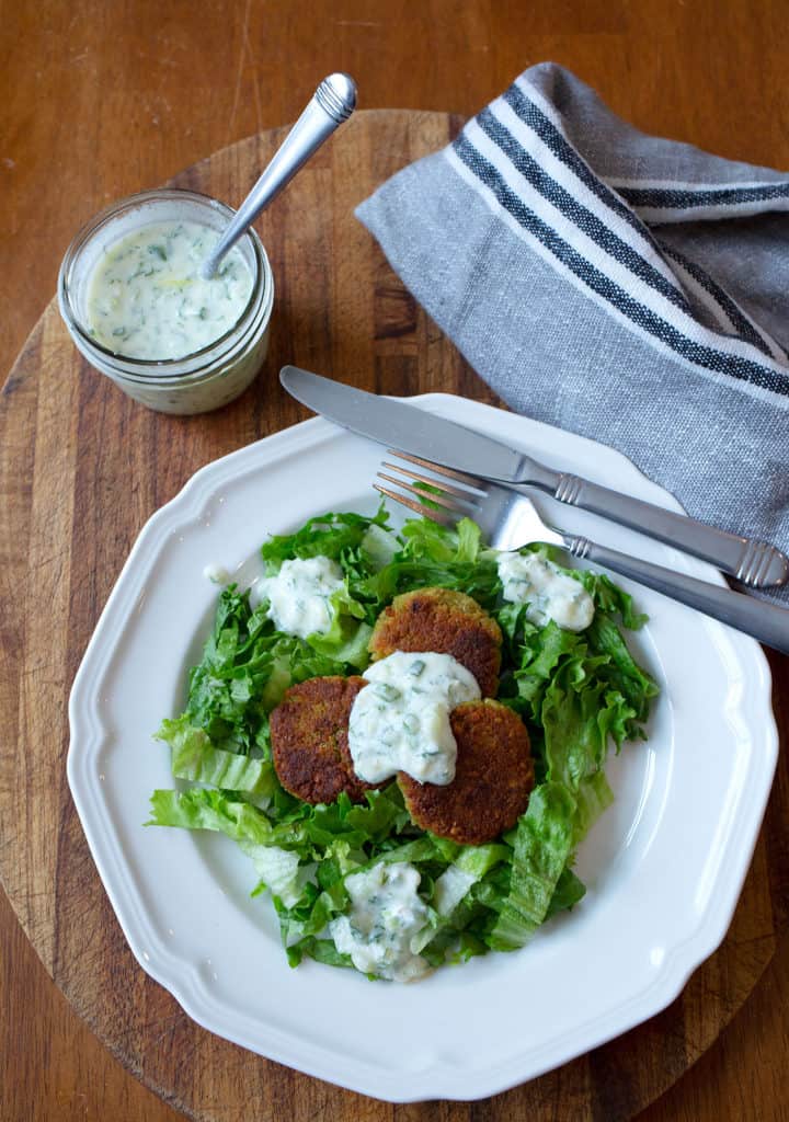 A plate of three falafel on top of salad greens with tzatziki sauce on top