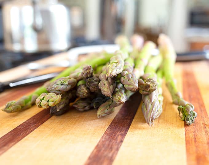 There are about 20 spears of fresh asparagus laying together on a cutting board.