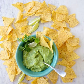 Bowl of guacamole garnished with lime wedge and cilantro surrounded by chips