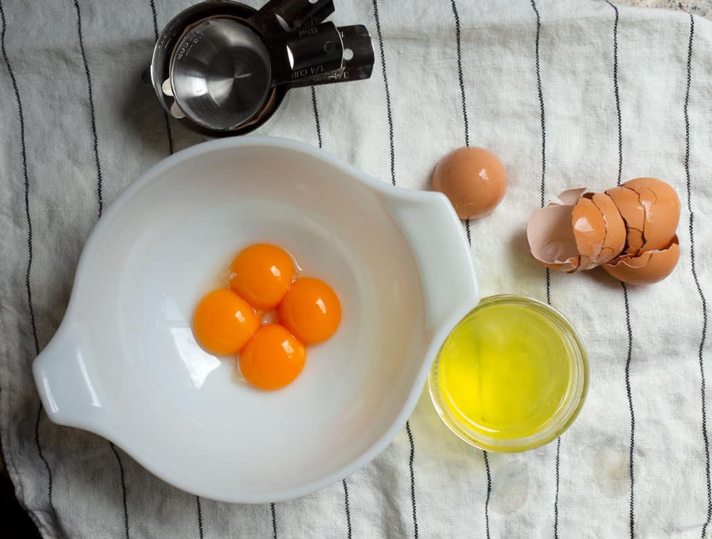 four egg yolks in a milkglass bowl with eggshells to the side