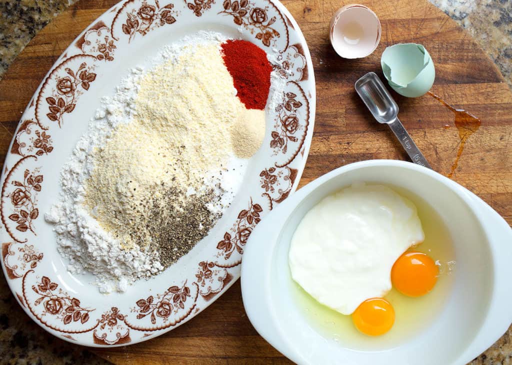 Eggs and buttermilk in one bowl and flour mixture on a platter