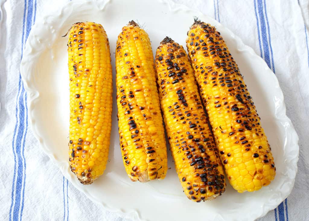 Grilled corn on the cob on a white platter