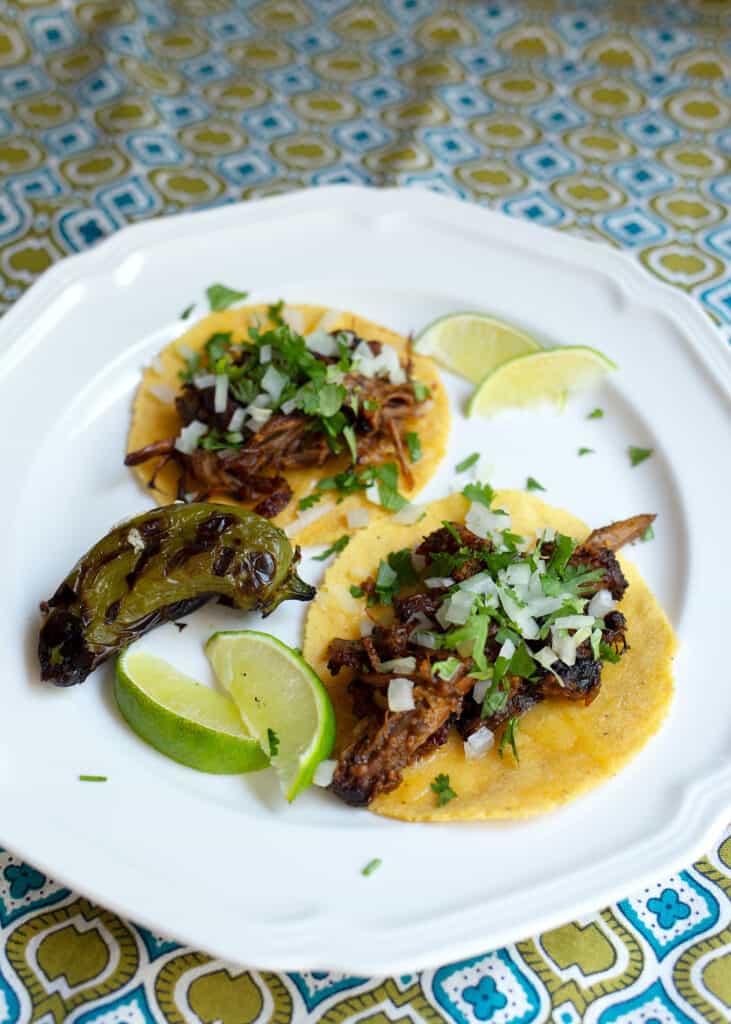 Two braised pork tacos on white plate with limes