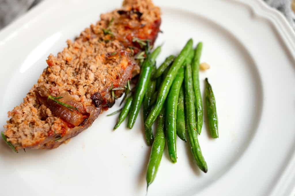 A slice of meatloaf and some sauteed green beans on a white plate