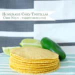 A stack of homemade corn tortillas with lime wedges and a jalapeno
