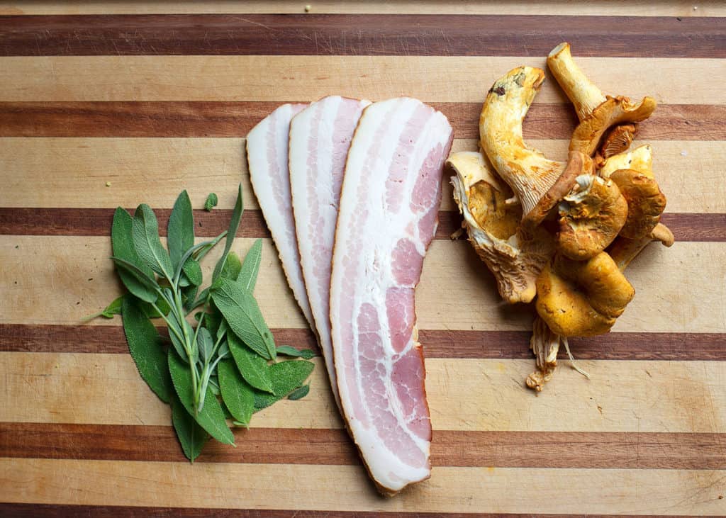 Fresh sage, bacon strips, and chanterelles on a cutting board