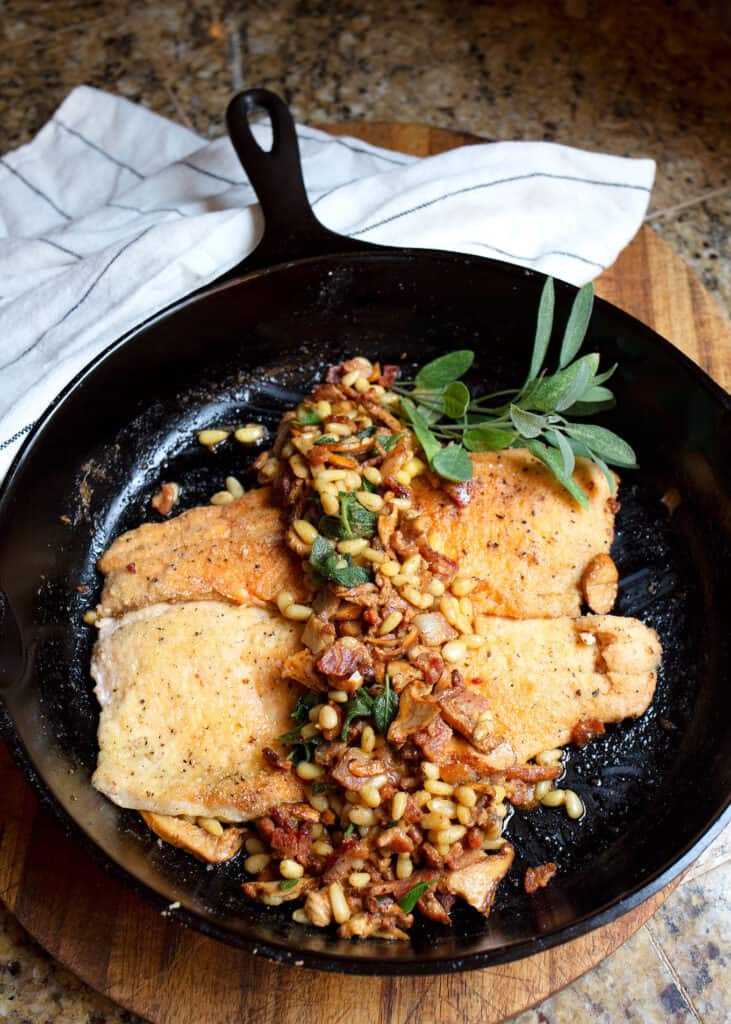 Two trout fillets in a cast iron skillet with the chanterelle sauce spooned over the top