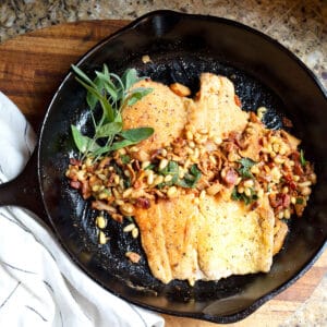 Cast iron skillet with trout topped with bacon, pine nuts, and sage