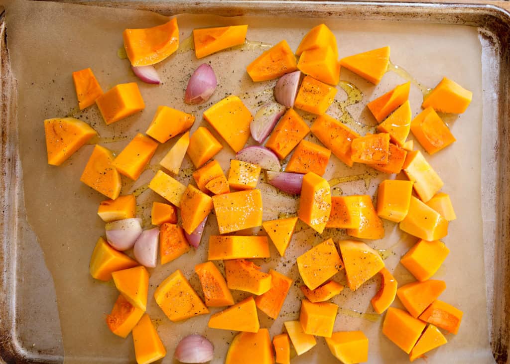 Chunks of squash and shallots on a parchment-lined baking dish