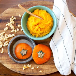 Roasted pumpkin in a bowl with pumpkin tops and seeds beside
