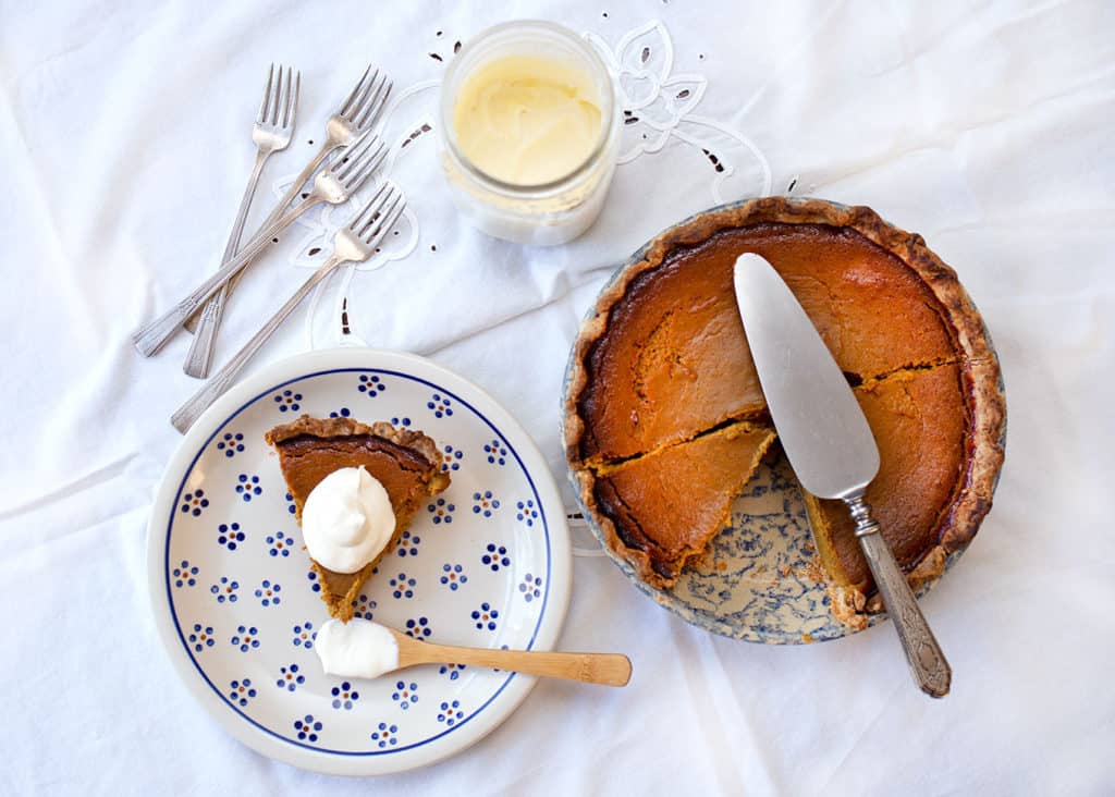 A piece of pumpkin pie on a plate with cream and the pie plate beside