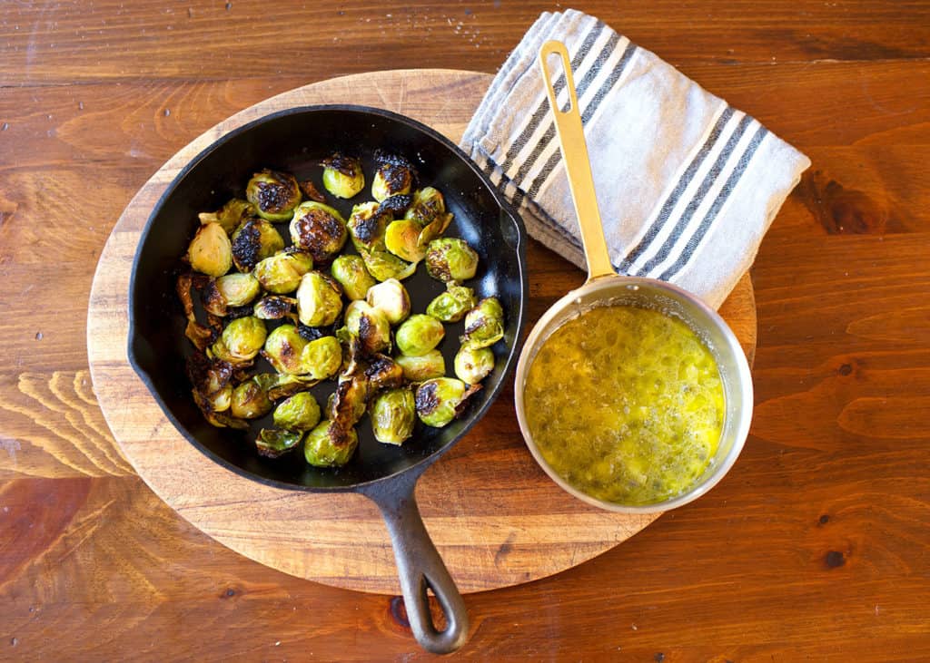 Brussels sprouts in cast iron skillet with the small pot of lemon caper sauce beside