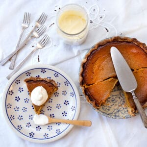 A slice of Real Food Pumpkin Pie on a plate with a dollop of cream on it sitting beside the whole pie