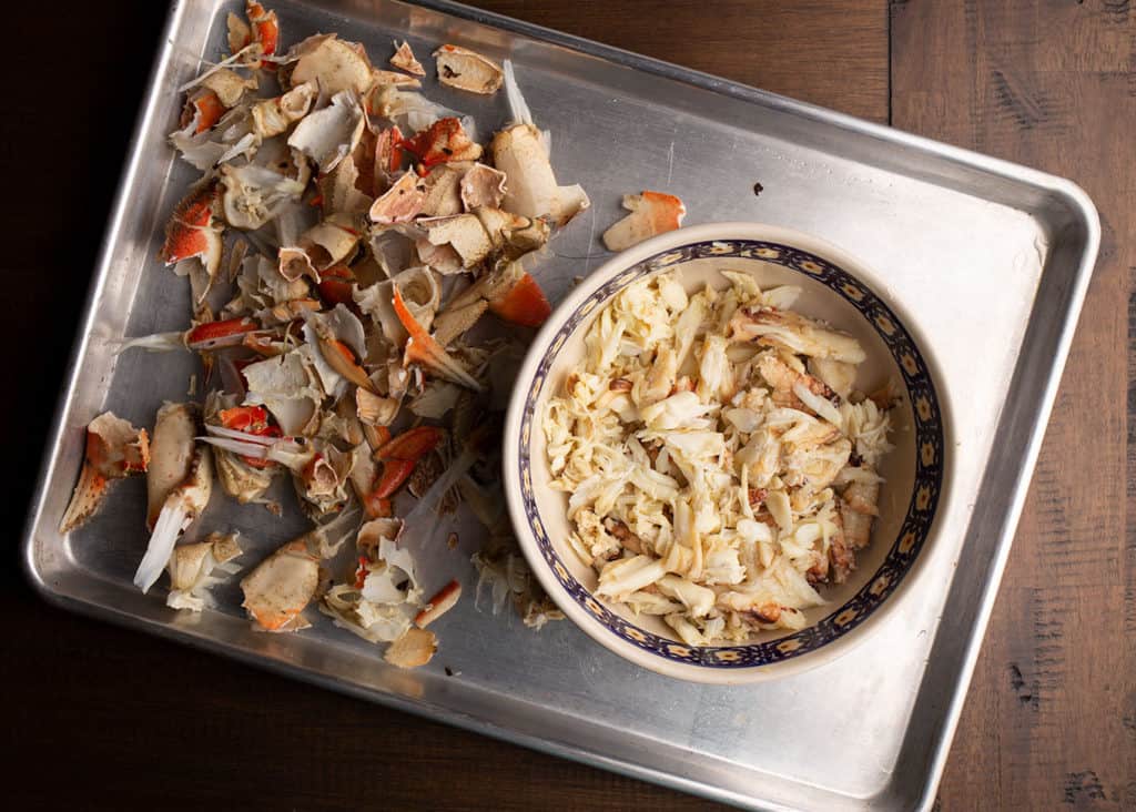 Bowl full of cracked Dungeness crabmeat and the shells laying on the side