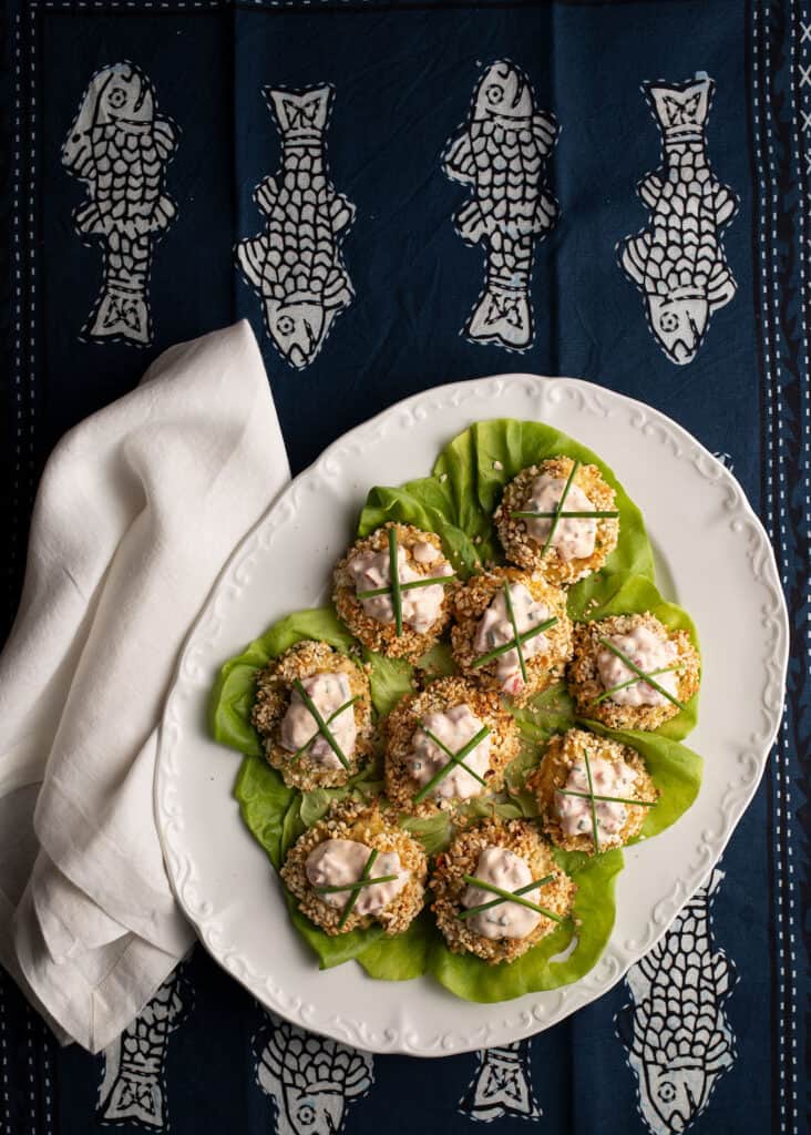 Crabcakes on a lettuce-lined white platter with a white linen napkin beside all on a navy blue cloth