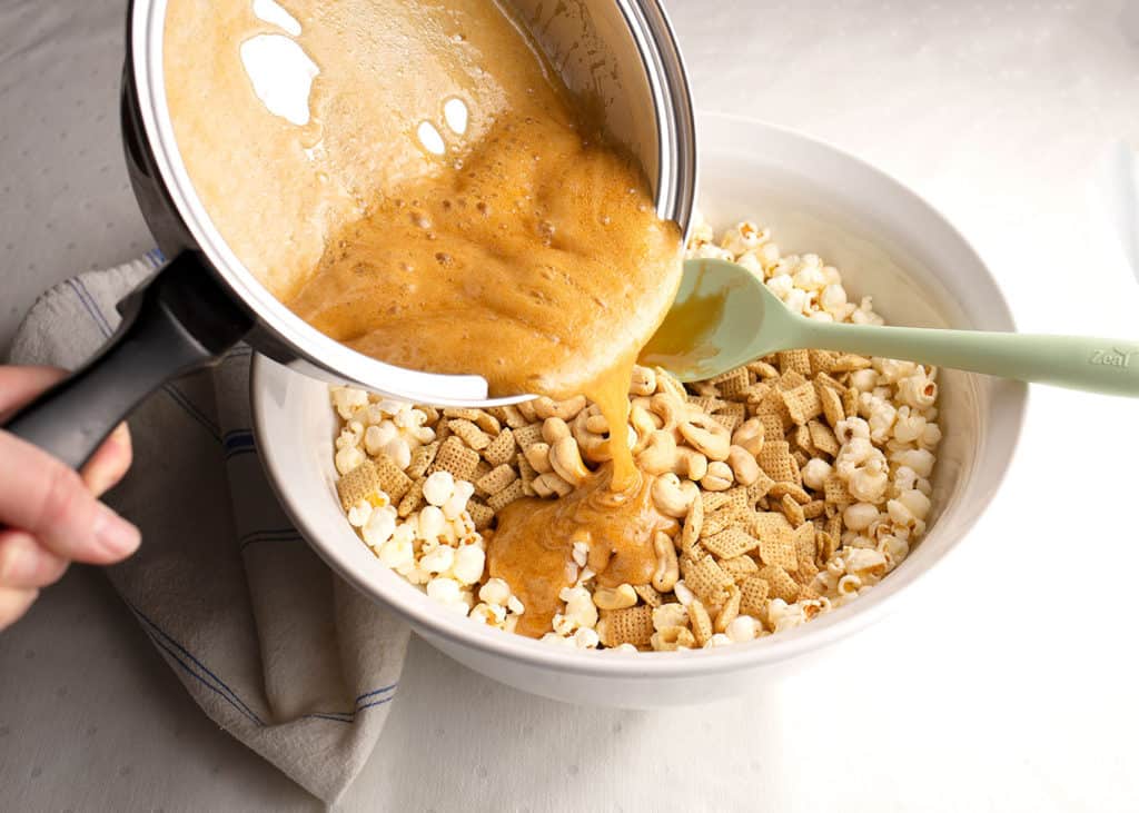 Caramel being poured over the popcorn, chex, and cashews