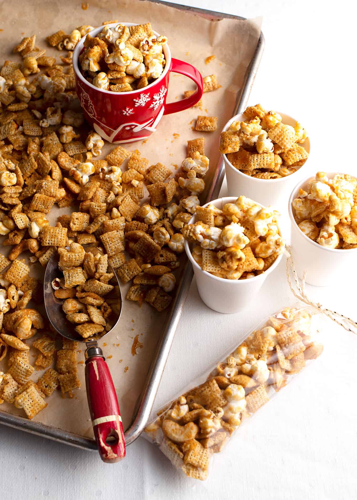 Three paper cups of Salted Caramel Cashew Corn sitting next to the baking sheet with a scoop