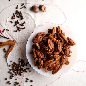 A bowl of Sugar and Spice Pecans with whole spices laying around on the table