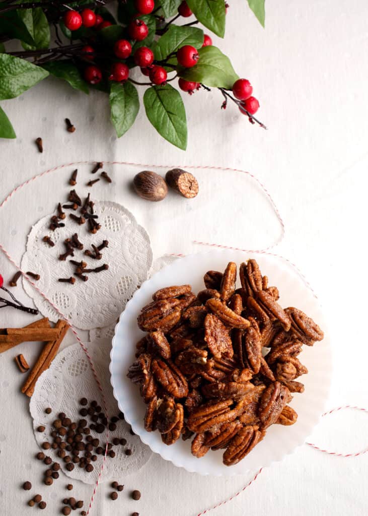 A bowl of Sugar and Spice Pecans with whole spices laying around on the table