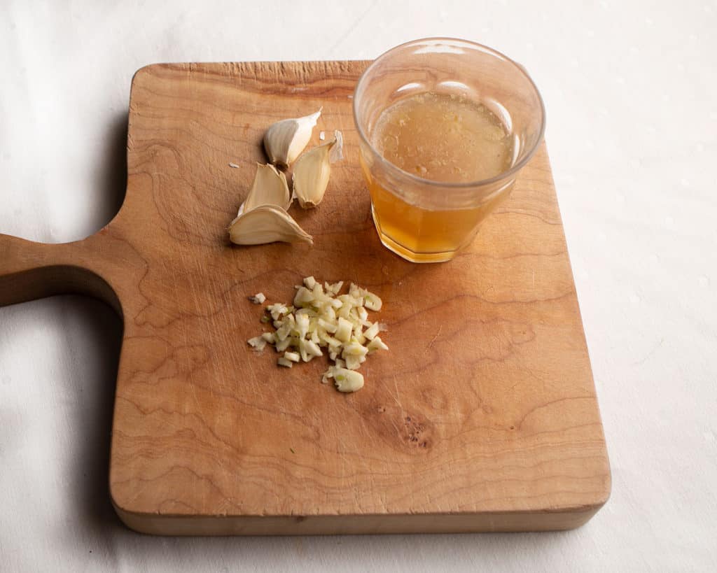 Chicken Broth in a cup and garlic on the cutting board for the sauce