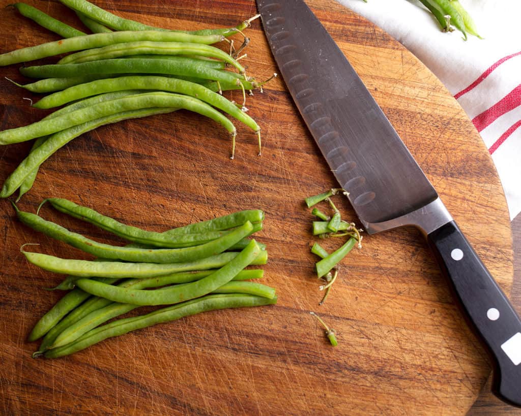 The tops trimmed off the beans with a chef's knife on a cutting board.