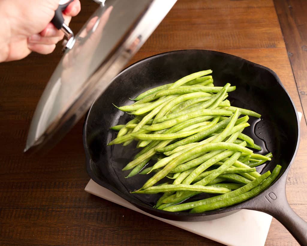 Cast iron skillet with green beans and water for steaming