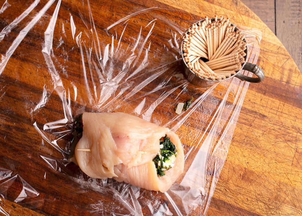 Rolled chicken with the filling and being held with a toothpick