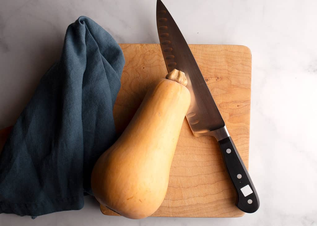 One whole butternut squash on a cutting board with a knife