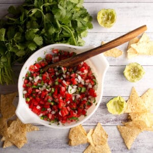 A white bowl full of fresh pico de gallo with a wooden spoon for serving