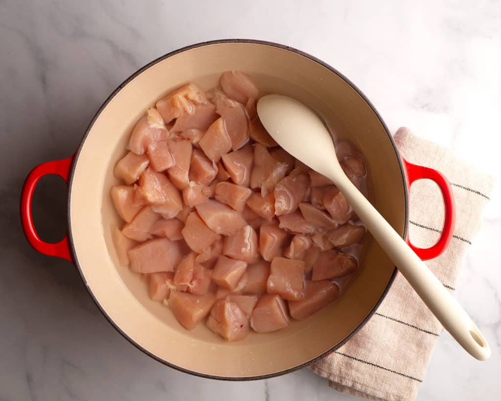 Cubed chicken covered in water in a large pot
