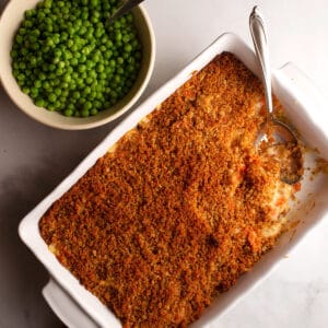 A casserole dish of Cheesy Chicken Casserole with a bowl of green peas beside