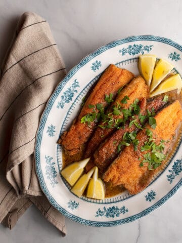 A blue and white platter with 4 trout fillets garnished with lemon wedges and parsley