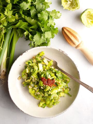 Bowl with Crunchy Celery Salad in it with a fork, a lemon reamer beside with green onions and cilantro