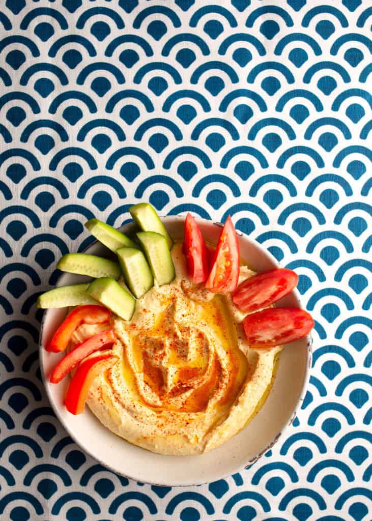 Plate of hummus drizzled with olive oil and accompanied by vegetables