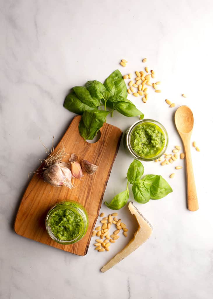 Two jars of pesto with fresh garlic, basil, and pine nuts scattered