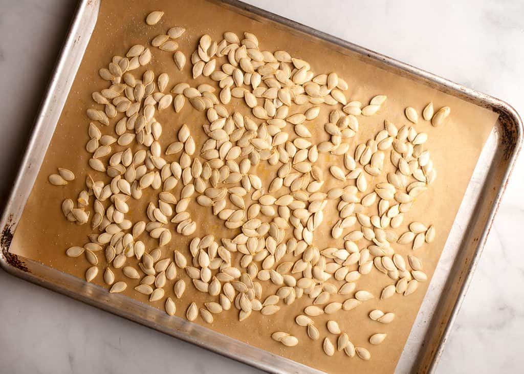 oiled and salted pumpkin seeds on parchment paper lined baking sheet