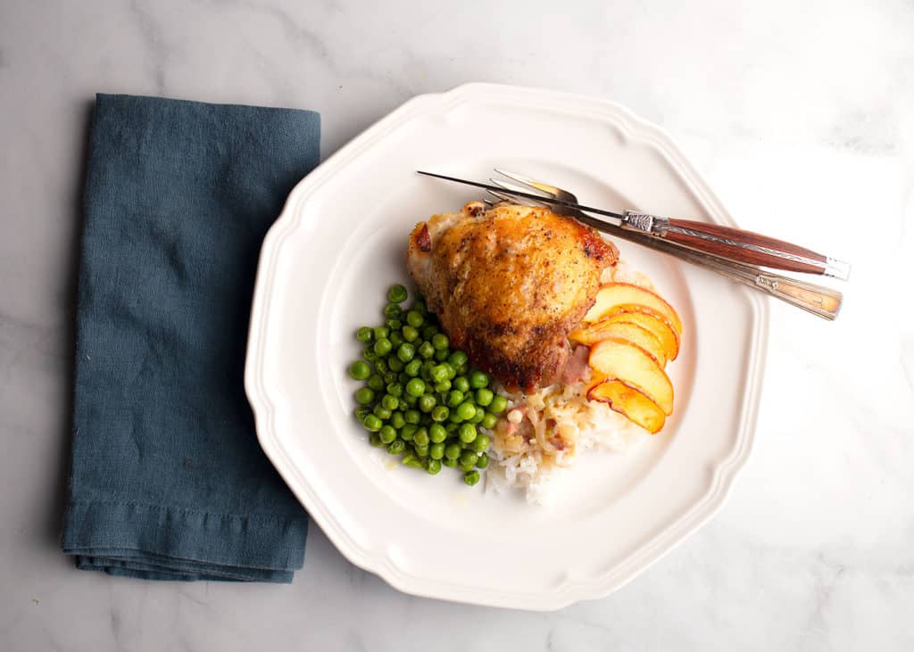 A plate of Apple Cider Braised Chicken with sauteed apples, rice, and green peas