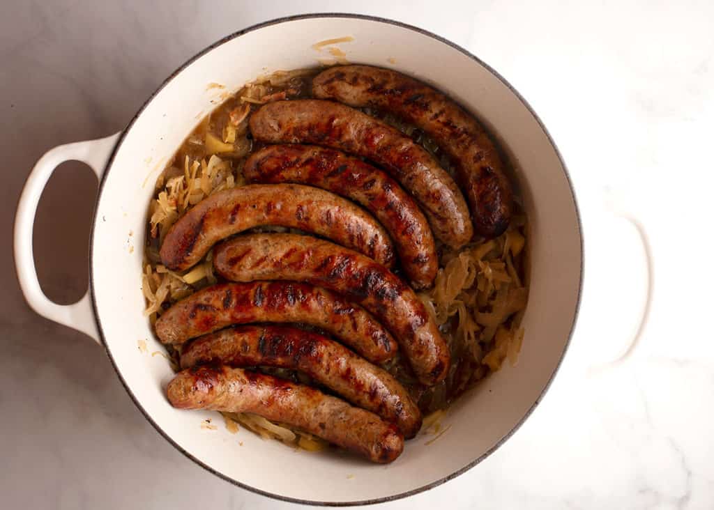 Grilled bratwursts on top of the sauerkraut in a large Dutch oven