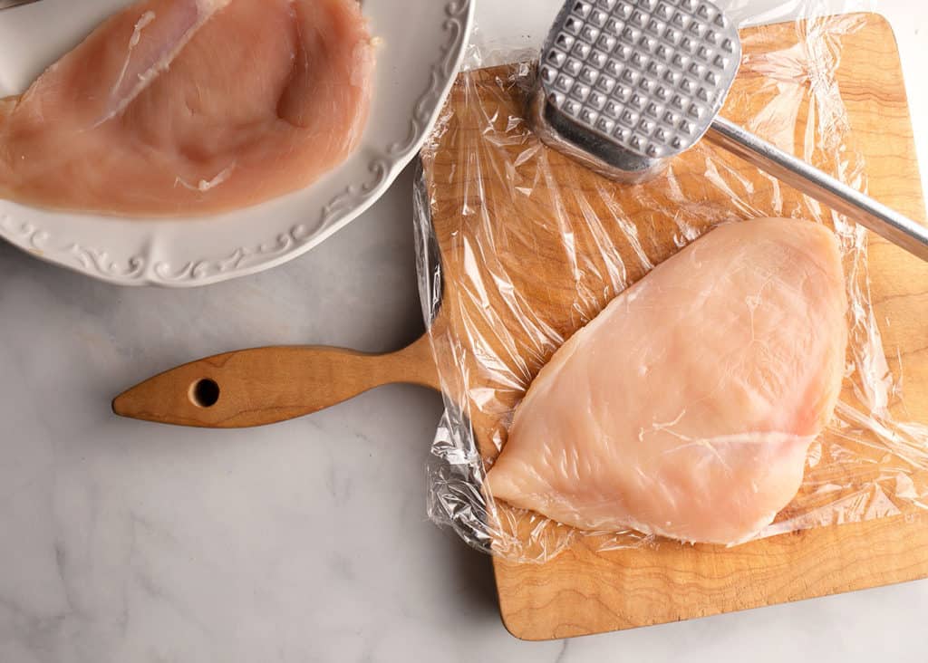 Skinless boneless chicken breast between plastic film pounded thin