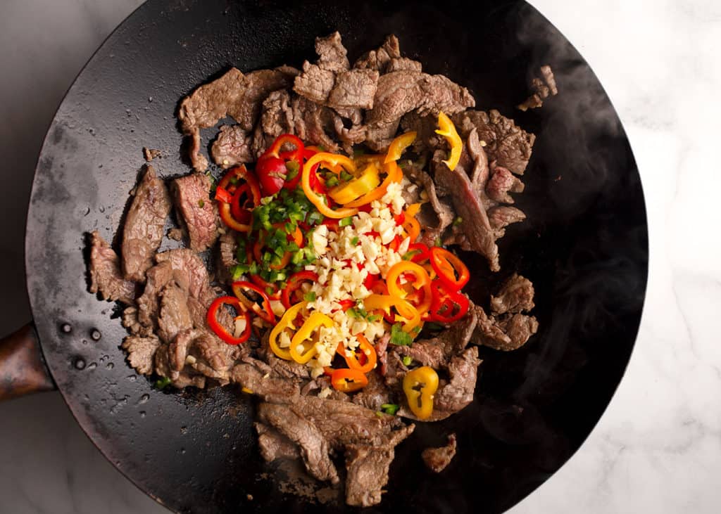 peppers, jalapeno, and garlic added to the cooked beef in the wok