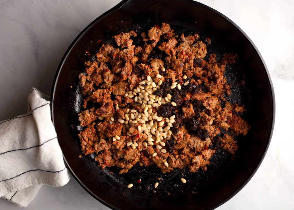 Browned sausage, pine nuts, and zante currants in a skillet