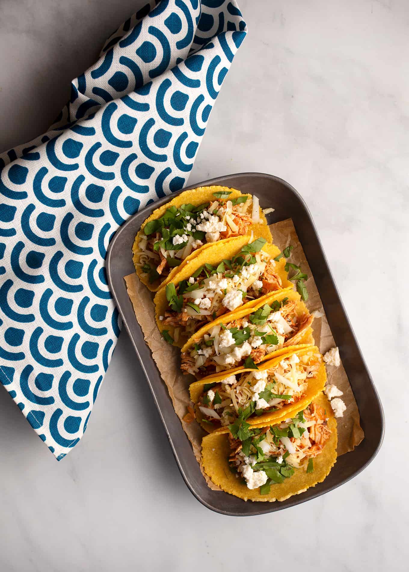 Five Chicken Tinga Tacos dressed with cilantro, salsa, and cheese on a pewter platter. 