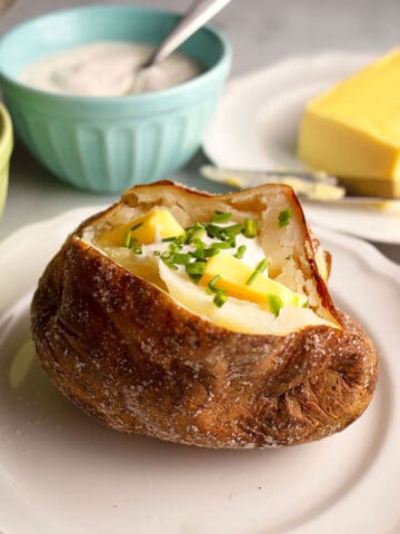 A baked potato (jacket potato) cut open with butter, sour cream, and chives in it.