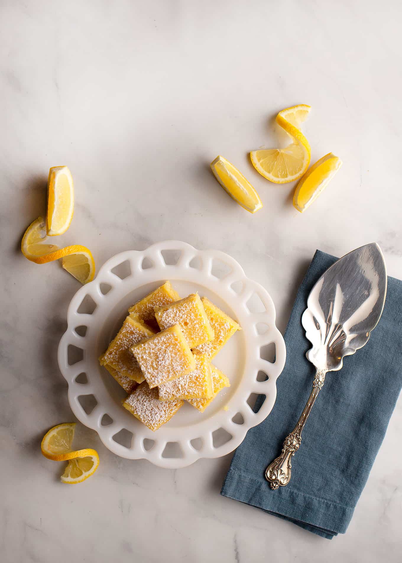 A stack of lemon bars on a vintage plate with some lemon slices on the table.