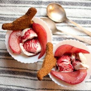 Two servings of Wine-Poached Pears in white dishes garnished with bird shaped cookies