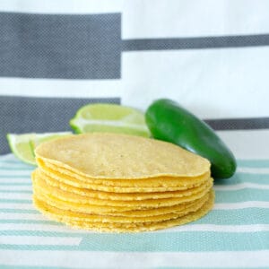 A stack of homemade corn tortillas with a sliced lime and a jalapeno beside