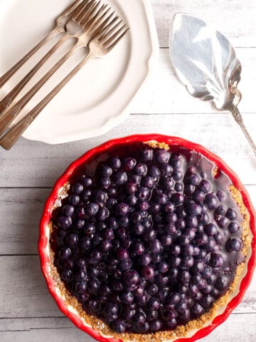 Whole Blueberry Cream Pie with a stack of plates with forks and pie server