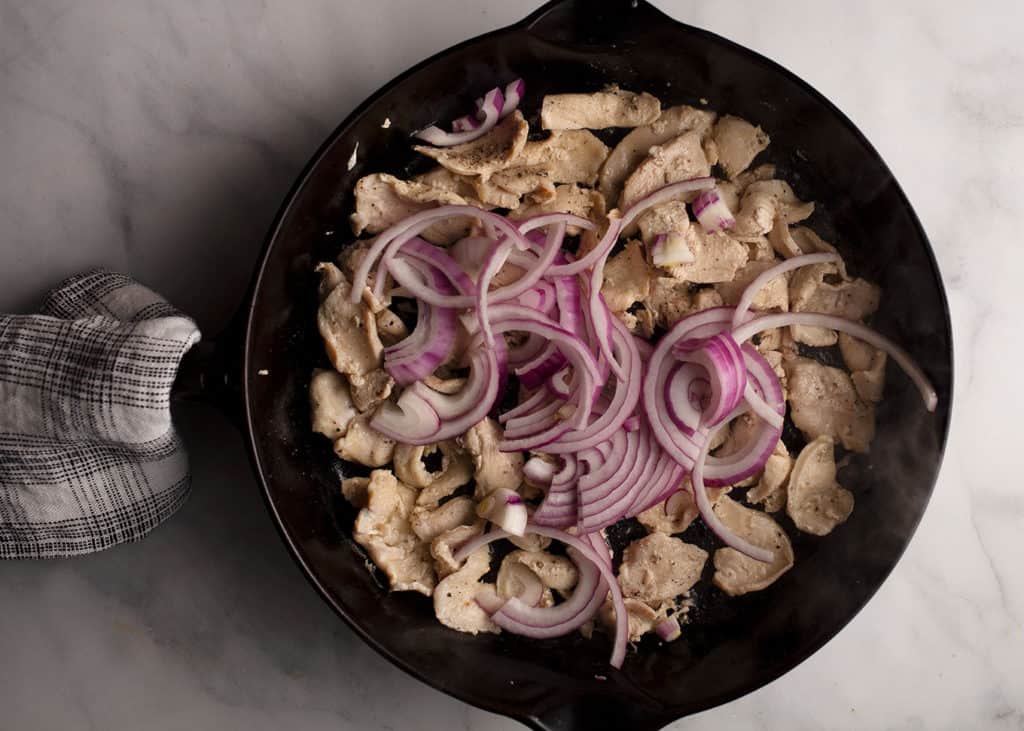 Chicken slices and red onion in the skillet