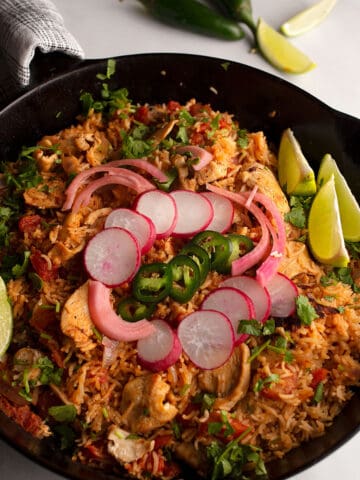 Cast iron skillet with Chipotle Chicken and rice in it, garnished with radishes, onions, and limes