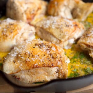 Close up view of a crispy chicken thigh in a skillet with the sauce and topped with parmesan cheese